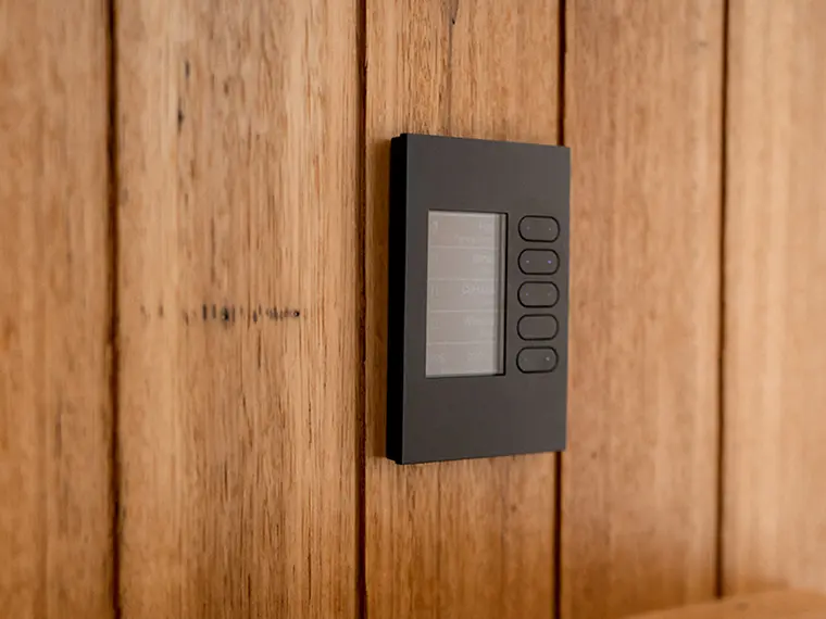 Black wall-mounted C-Bus panel with five buttons on a wooden wall.