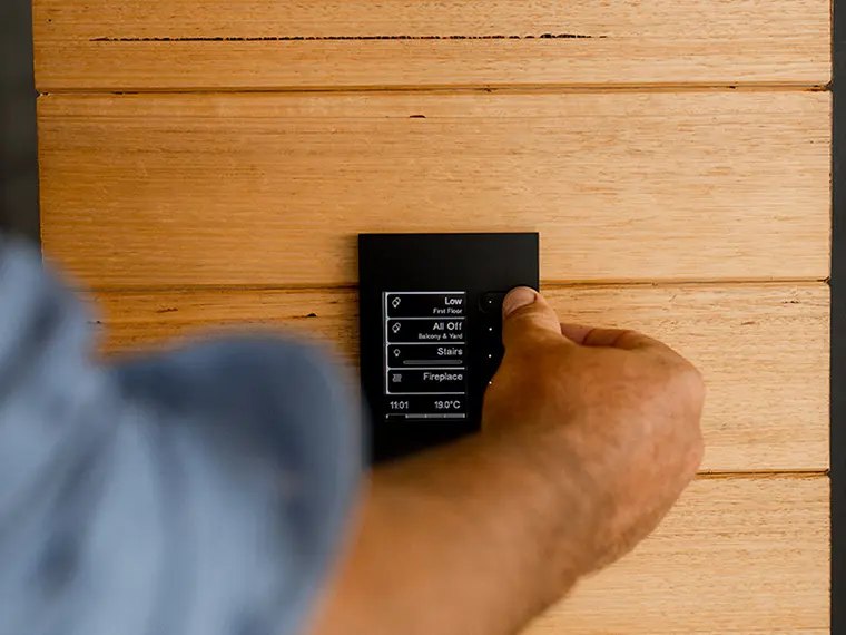 Hand adjusting a wall-mounted C-Bus touchscreen control panel for lighting and temperature.