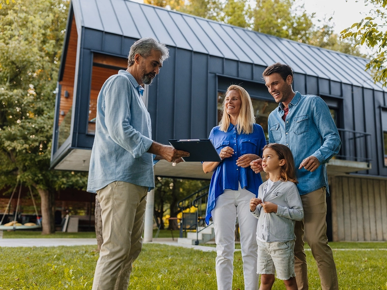 A family in front of a house as a man shows them a clipboard discussing home design details.