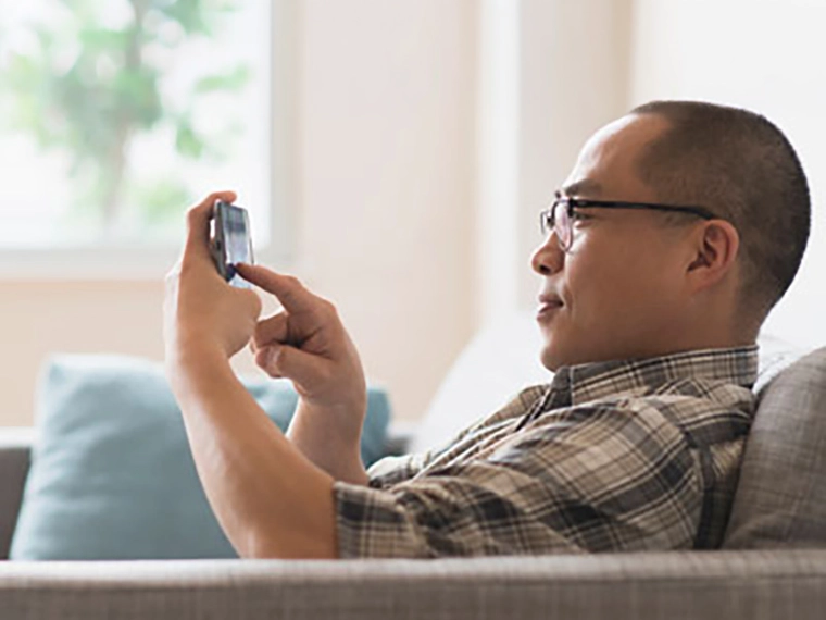 Person sitting on a sofa using a smartphone indoors.