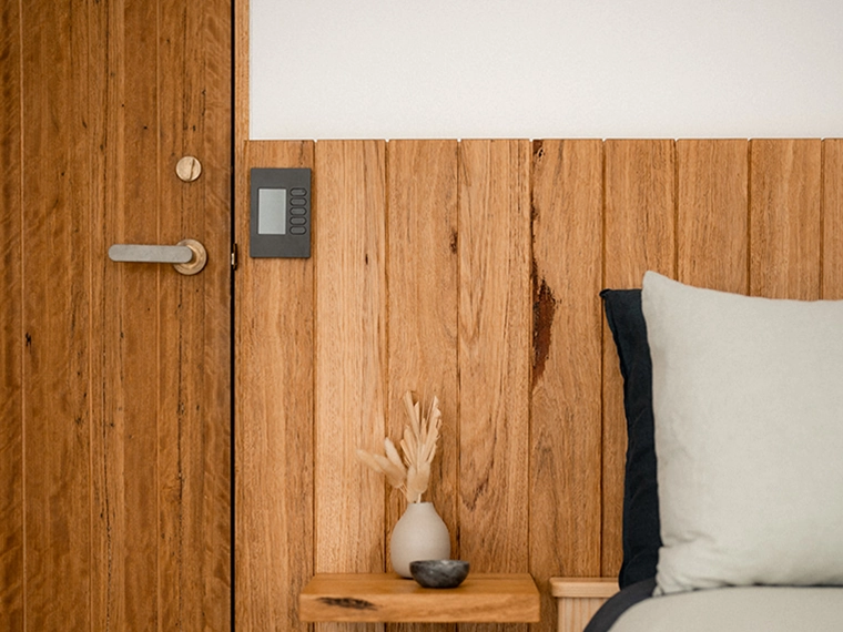 Wood wall with SpaceLogic C-Bus panel on bedside table in minimalist bedroom.