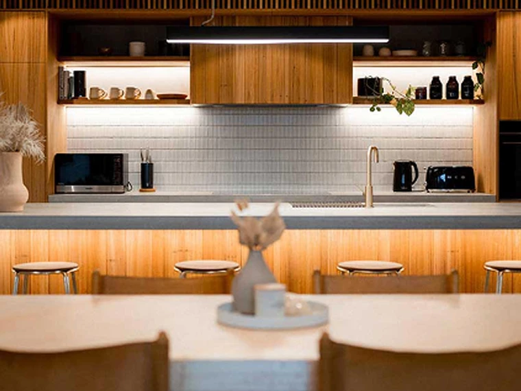 A warm, modern kitchen with wooden cabinetry, open shelving, and soft under‑cupboard lighting.