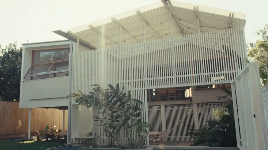 Modern two-storey home with large windows, timber shade slats, open entryway, and landscaping in front.