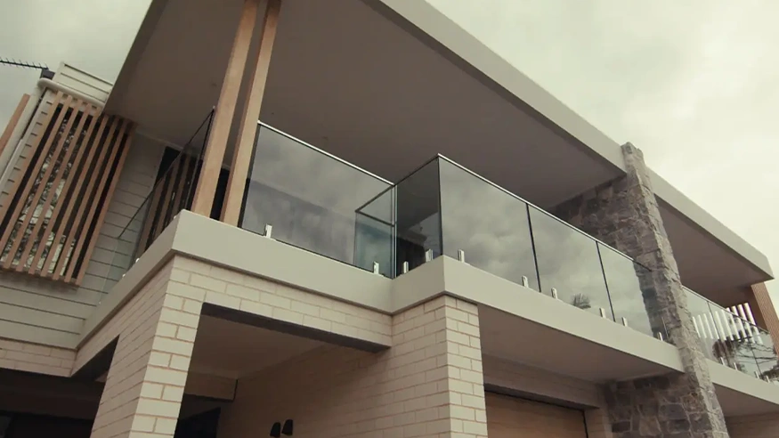 Modern multi-storey house with flat roof, glass balcony, light brickwork, timber slats, and stone detailing.