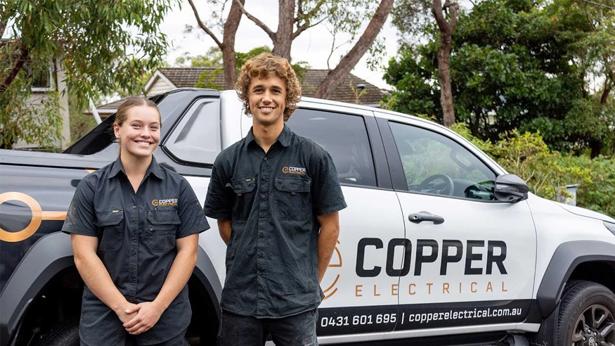 Two workers stand next to a truck carrying copper electrical components, preparing for their task ahead.