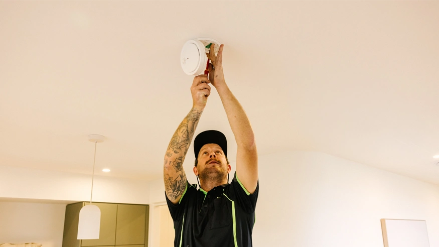 An electrician installing a Clipsal Smoke Alarm in a home kitchen.