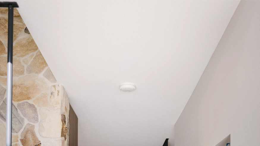 A Clipsal Smoke Alarm installed in the ceiling of a hallway.