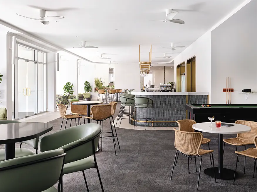 Modern lounge with tables, chairs, bar counter, pool table, and large windows letting in natural light.