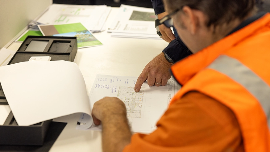 Two workers reviewing technical drawings on a desk.