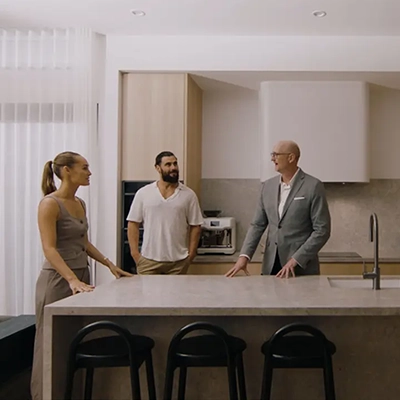 An interior designer discusses design with two people in a modern furnished kitchen space.