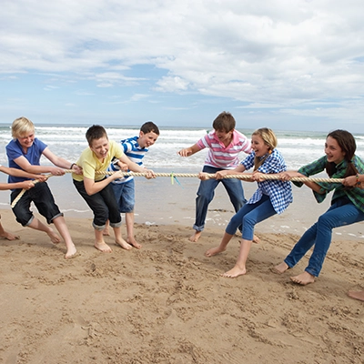 A group of teenagers play tug-of-war on a beach.