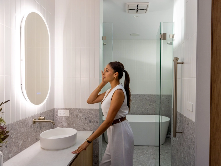 A woman in front of a mirror and sink in a modern bathroom.