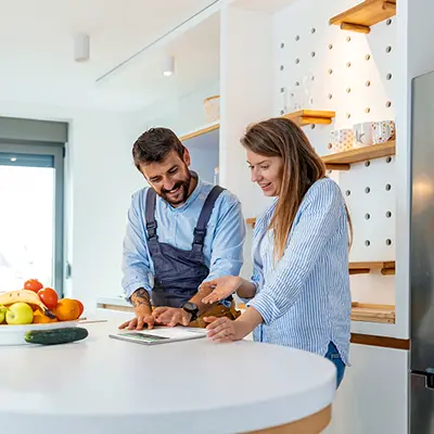 A man and a woman browse the Clipsal Digital Asset Toolkit on a tablet device in a modern kitchen.