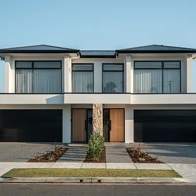 Modern white duplex with black garage doors, wooden front doors, large upper windows, and small landscaped front yards.