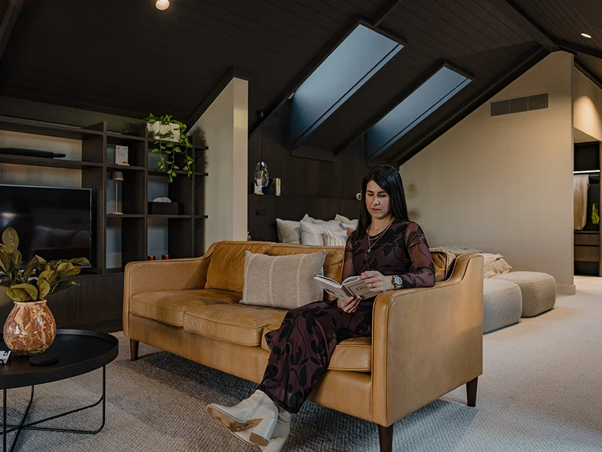 A woman sitting in a cosy, warm living room with a book in hand.