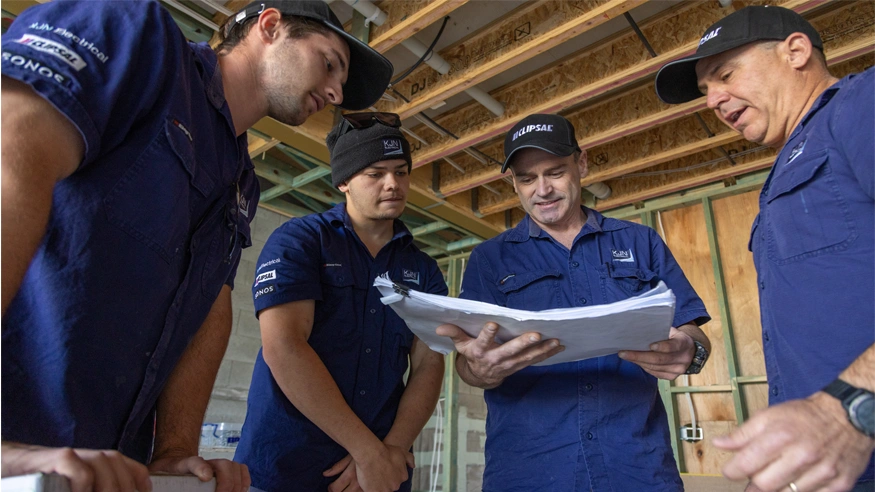 Electricians from KJN Electrical reviewing an electrical plan in a construction site.