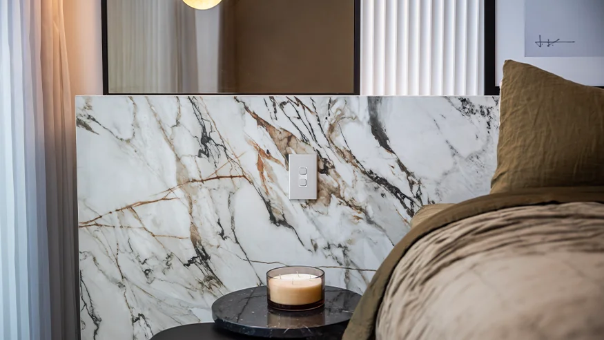 Iconic switch installed on a marble wall beside a bed with a candle on a small black side table.