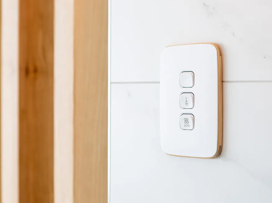 Vertical 3-gang Clipsal Iconic Essence switch with fan and temperature buttons on a white tiled wall.