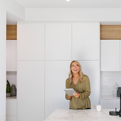 Person holding a tablet in a modern white kitchen with minimalist cabinets and marble countertop.