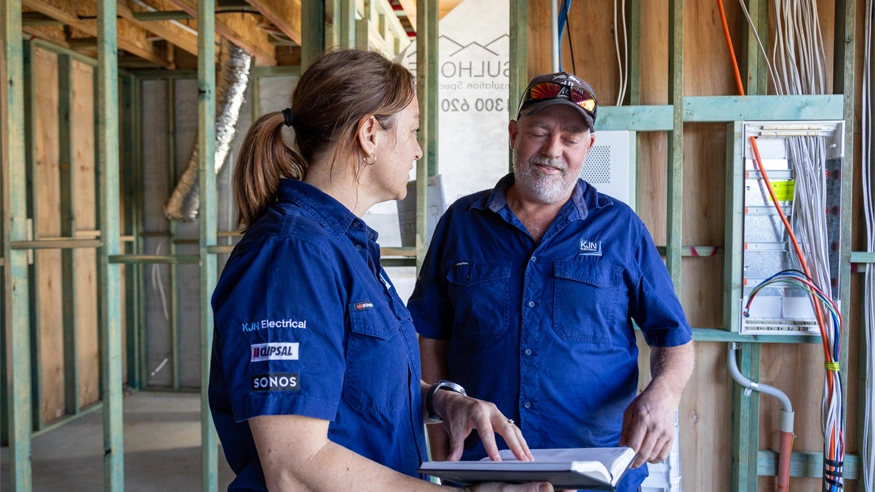 Two electricians from KJN Electrical standing in a construction site, both dressed in Clipsal-branded shirts.