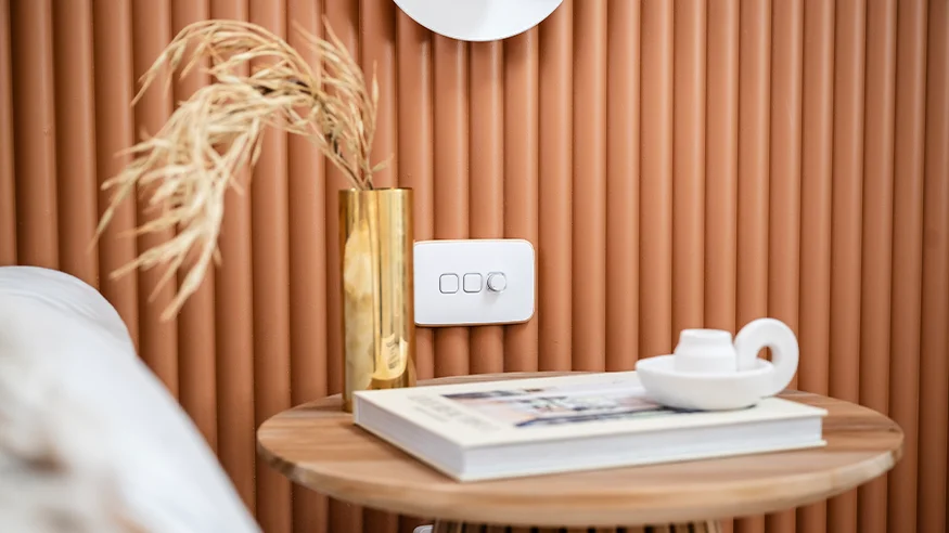 Iconic switch on a wall beside a round wooden side table with a gold vase and books.