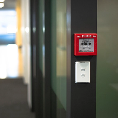 Red fire alarm and white Pro series switch mounted on a dark wall in an office hallway.