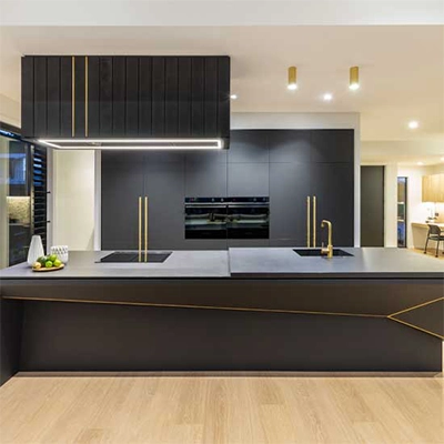 Modern black kitchen with gold accents, large island and built-in appliances.