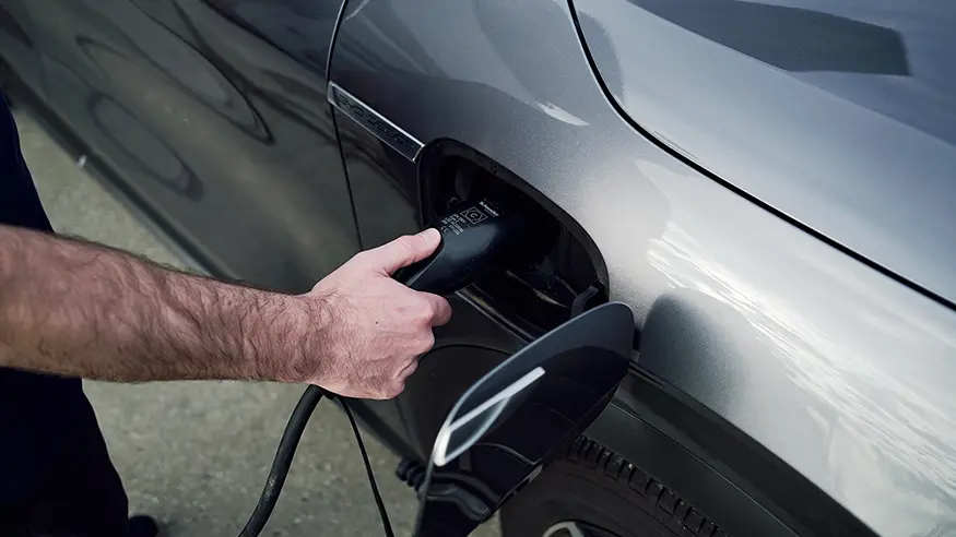 Hand plugging a charging cable into an electric vehicle’s port on a metallic grey car.
