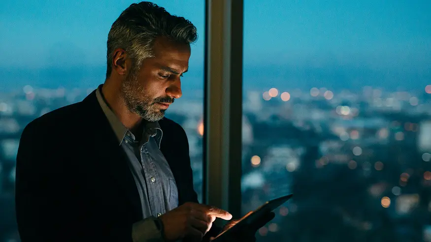 A man using a smartphone in front of an office building window.