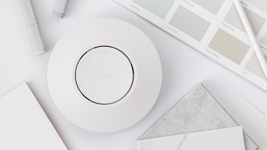 White smoke alarm on a flatlay with paint swatches, tiles, and design tools.