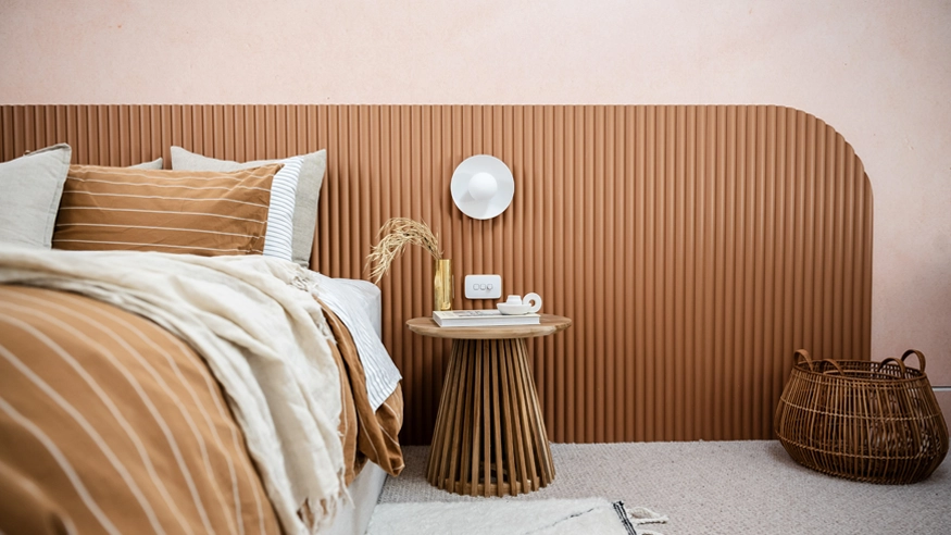 Bedroom with a wooden headboard, neutral-toned bedding, and a side table with an Iconic Essence switch beside it.