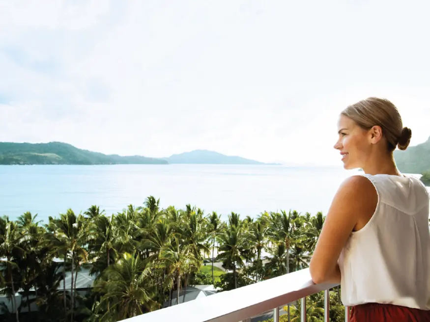 Person on balcony overlooking ocean and palm trees.