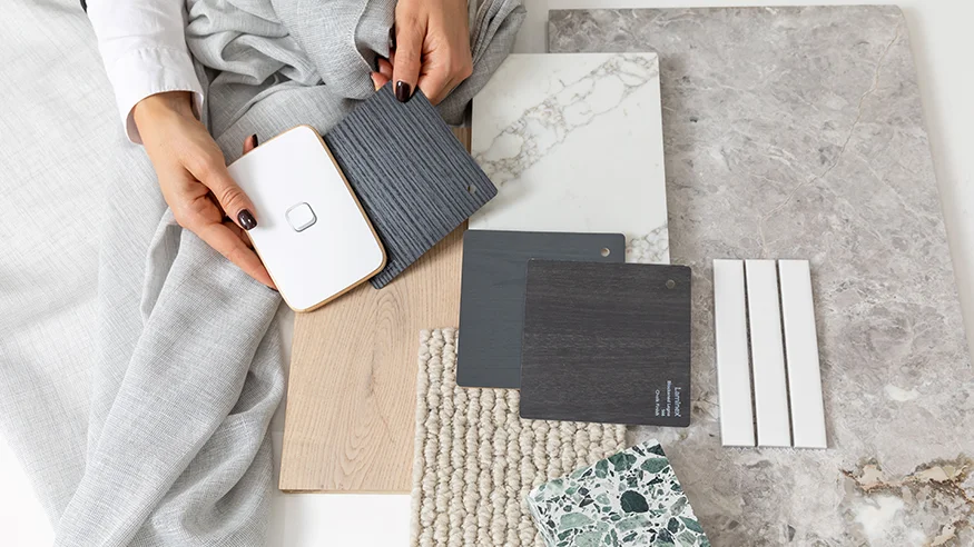 Hands holding colour and material samples, including a Iconic switch, fabric swatches, and stone tiles.
