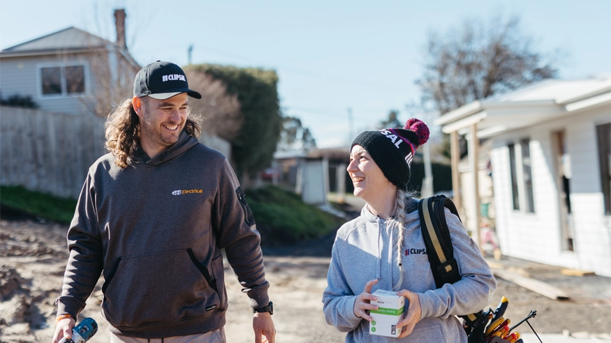 Steph and Chris Gee walking together while wearing Clipsal-branded clothing and carrying Clipsal products.