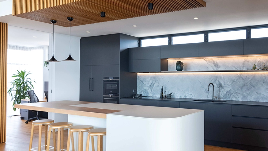 Modern kitchen with dark cabinets, marble backsplash, white island, bar stools, and warm under‑cabinet lighting.