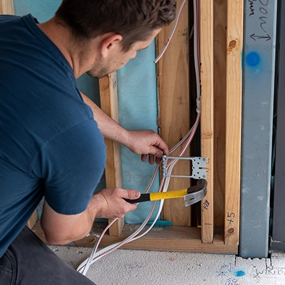 Person installs mounting accessory in wooden frame wall using hammer.