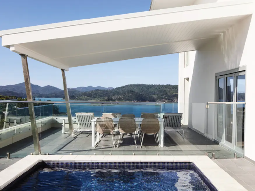 Outdoor patio with dining table, chairs, and pool overlooking a scenic lake and mountains.