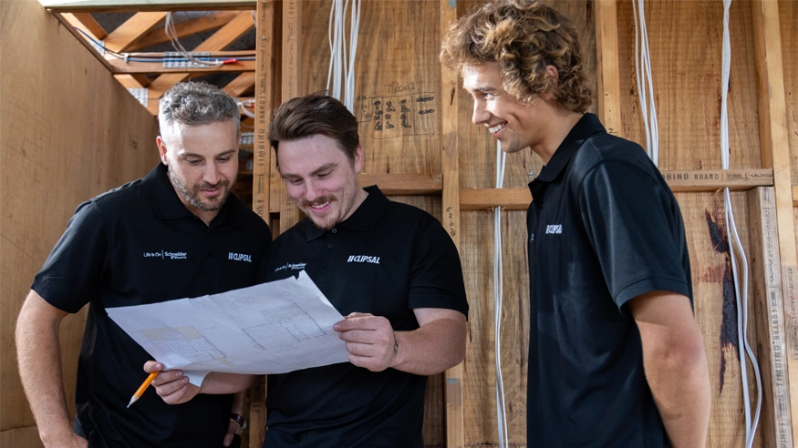 Three men in black shirts examine a blueprint together.