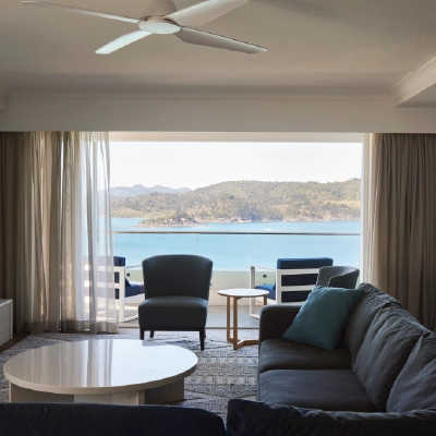 Living room with ocean view, featuring a ceiling fan, sofa, coffee table, and balcony with chairs.