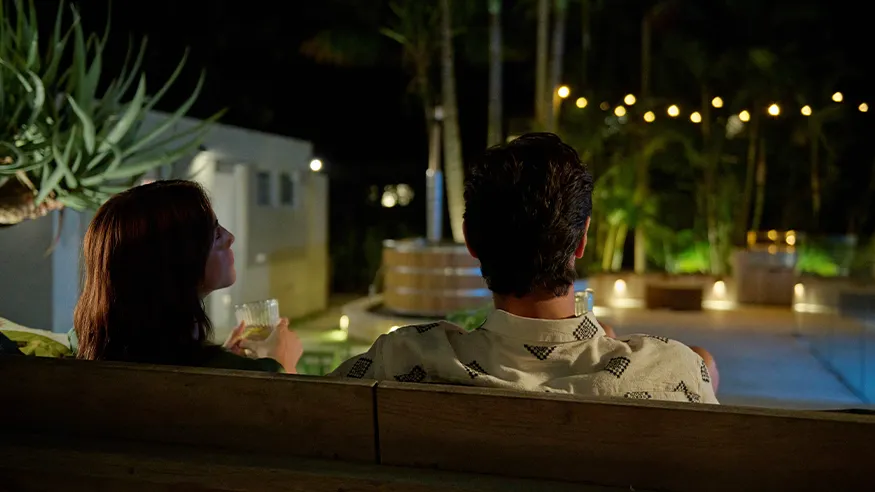 A couple relaxing while viewing Wiser Smart Home-automated lights by the poolside at night.