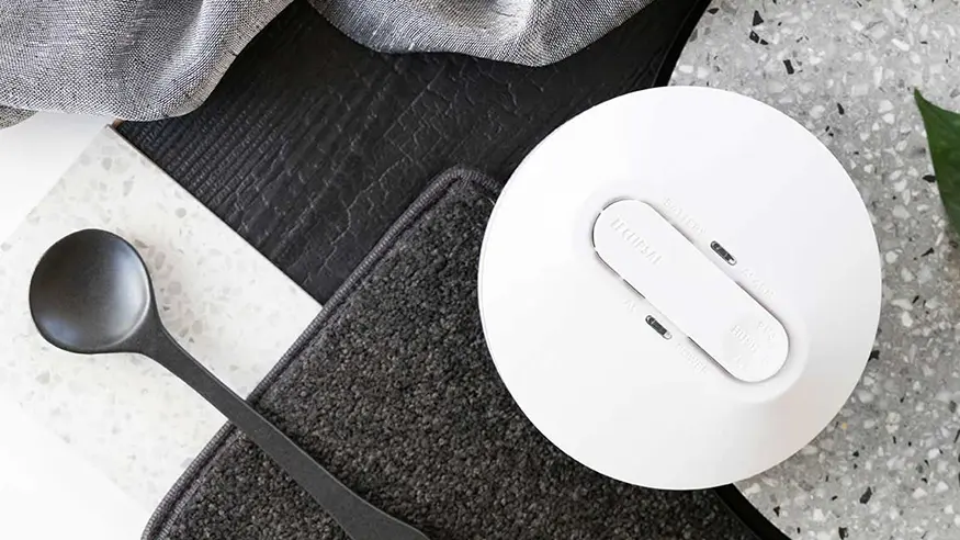 Flatlay of a round white smoke alarm placed among kitchen textiles.