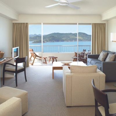 Modern living room with ocean view, beige furniture, and a balcony with chairs.