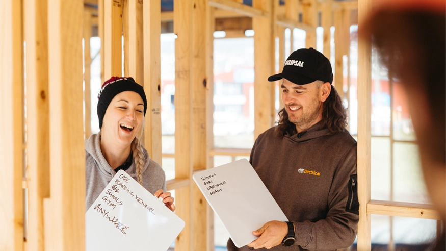 Steph and Chris Gee from Gee Electrical laughing while holding whiteboards.