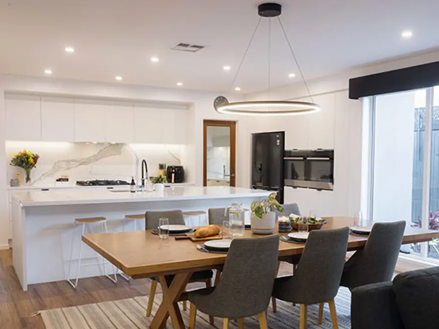Modern kitchen-dining area with circular ceiling light above a wooden table, white cabinets, and marble backsplash.