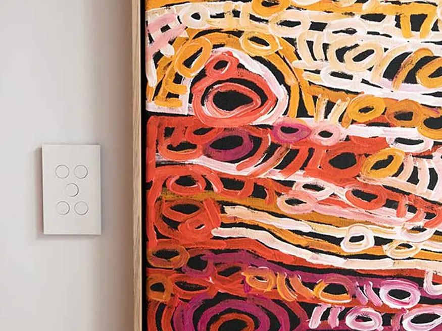 Saturn Zen push button switch in Zen White colorway mounted beside a vivid abstract painting.