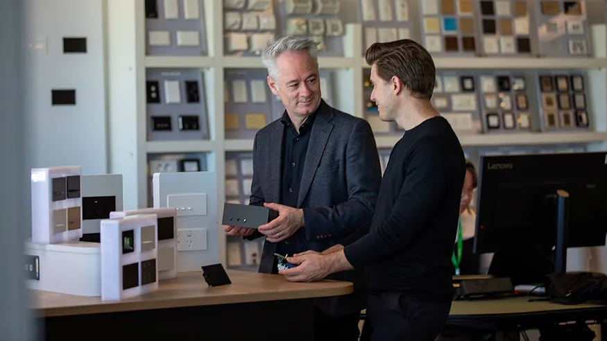 Two people discussing modern light switch panels in a showroom with sample displays on the wall.