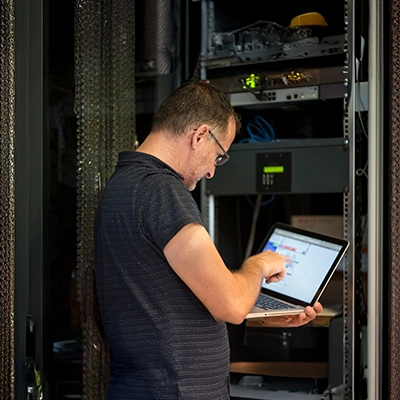 Person using a laptop while working on server equipment in a data centre.