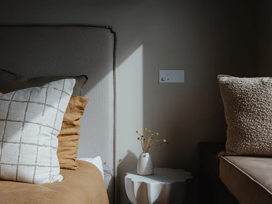 A Clipsal Solis switch installed next to a bed in an earthy-toned bedroom.