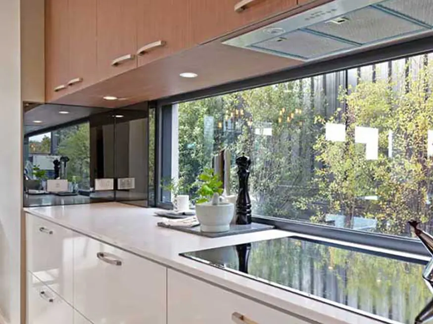 Modern kitchen with white and wood cabinets, black cooktop, and natural light from large window over the counter.