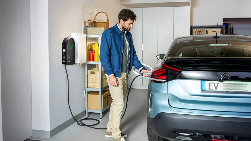 A man plugs his blue electric vehicle into a wall-mounted Schneider Charge Pro EV Charger in his garage.
